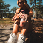 Person sitting outdoors holding a pink smoothie cup with 'Clean Eatz branding.